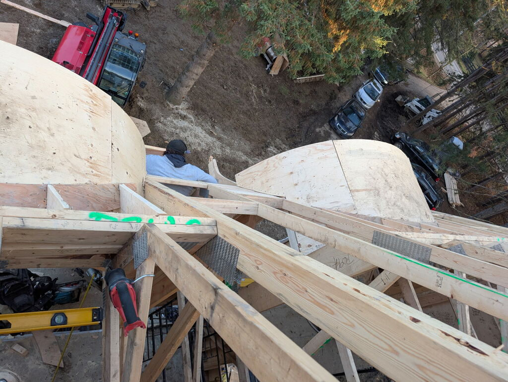 a worker from above documents a worker below, installing fascia along the perimeter of the roof's end