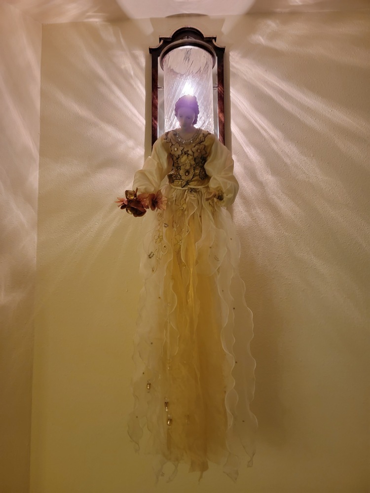 a doll or Christmas ornament that looks like an angel hanging from under a light